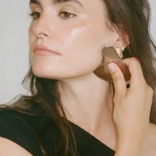 Bronze-toned facial massage tool with a smooth, curved surface and textured edge