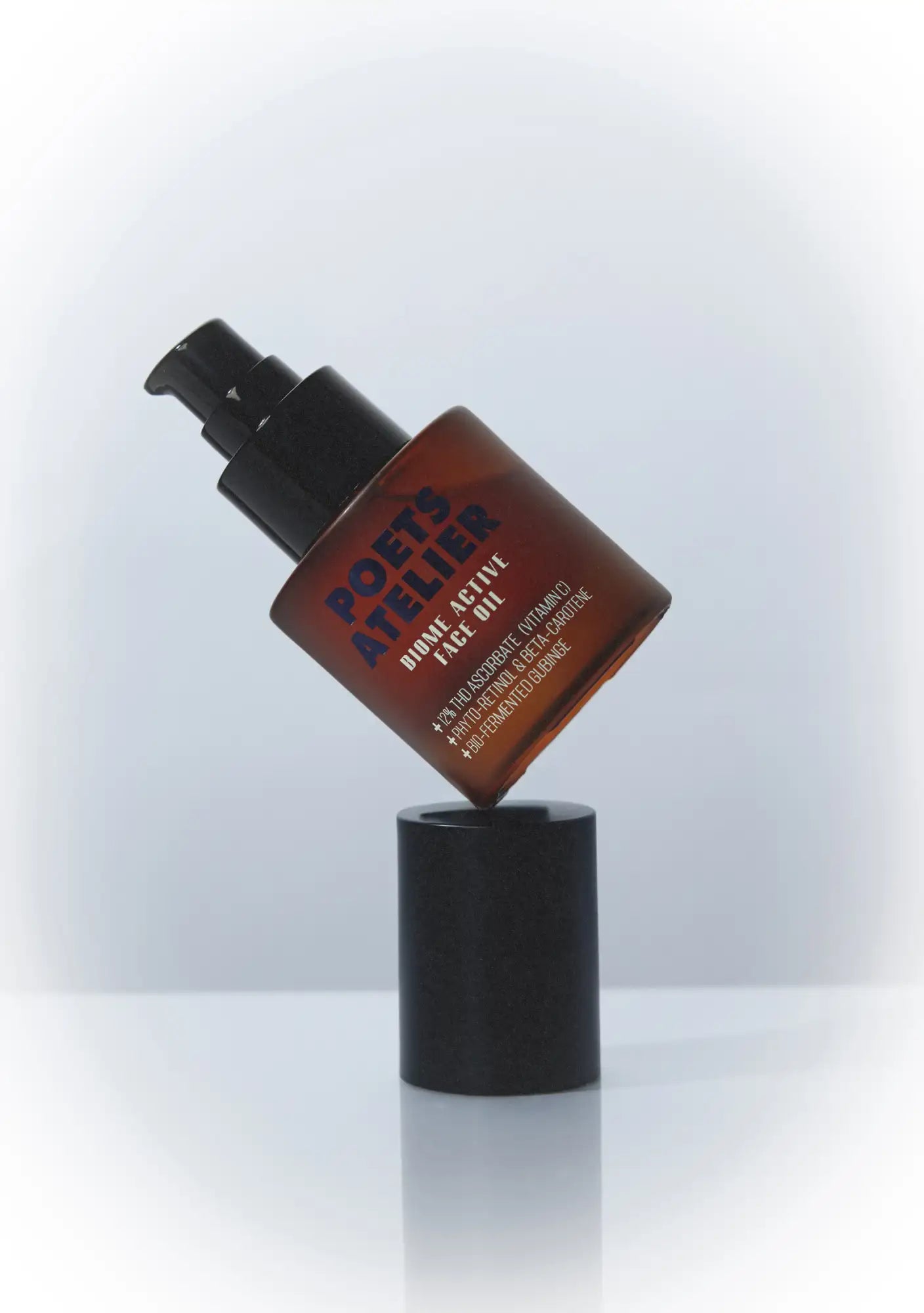 A sleek amber glass bottle of poets atelier bioactive face oil with a black pump dispenser, featuring bold blue and white text on its label.