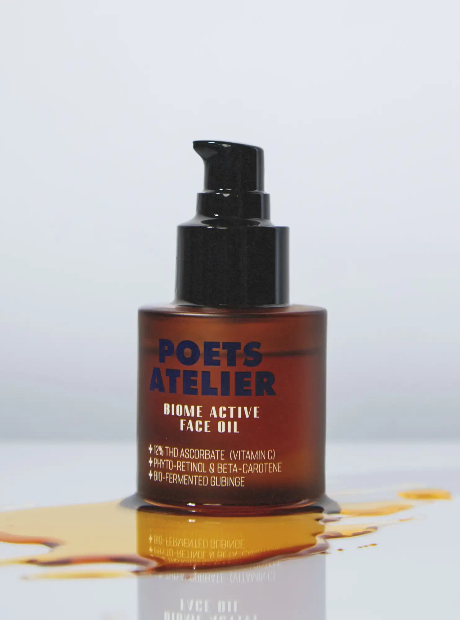 A sleek amber glass bottle of poets atelier biome active face oil with a black pump dispenser, featuring a minimalist label and droplets of oil spilling around its base.