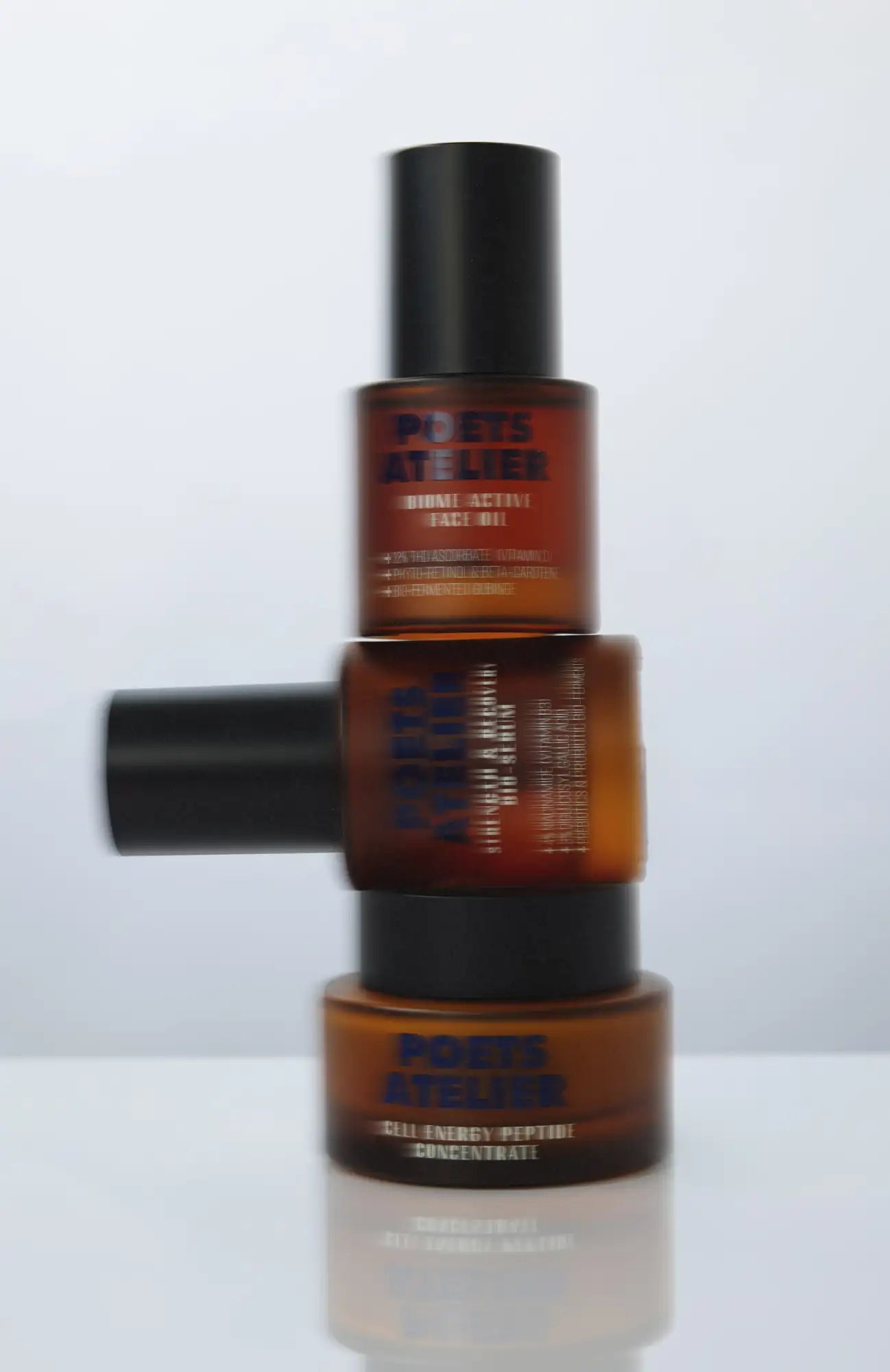 Stacked amber glass bottles with black caps, labeled ’poets attelier’ and featuring product names like ’bio energy peptide concentrate.’